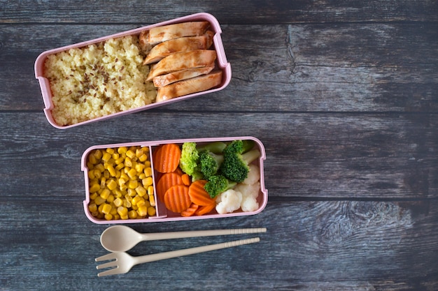 Schul-Lunchboxen mit Huhn, Brei, frischem Gemüse auf dunklem Holzhintergrund. Draufsicht. Platz für Text