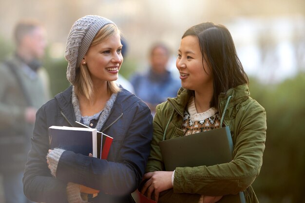 Foto schulbücher und gespräche mit freundinnen im freien auf dem campus zusammen zum lernen oder zur entwicklung hochschulbildung oder universität mit einem jungen studenten und einer besten freundin, die sich in der pause unterhalten