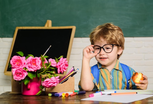 Schulferienhungriges Kind, das Apfel im Klassenzimmer isst, süßer Schuljunge zur Mittagszeit im Klassenzimmer