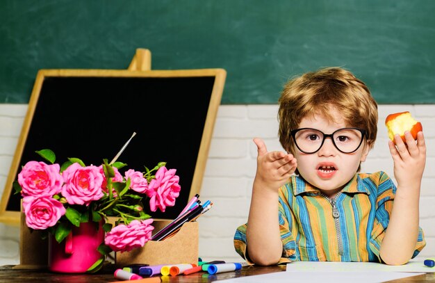 Schuljunge, der mit Apfel zu Mittag isst. Gesundes Essen für Kinder. Kleiner Schüler während der Mittagspause im Klassenzimmer.