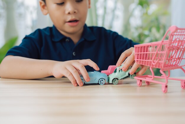 Schuljunge, der zu Hause mit Spielzeugauto auf einem Tisch spielt.