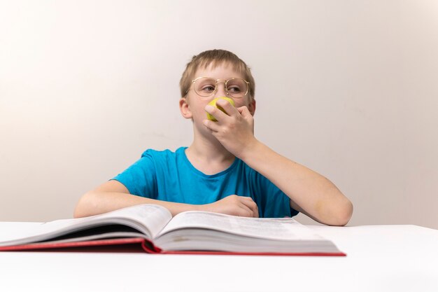 Schuljunge isst Apfel und liest Buchjunge mit Brille macht seine Hausaufgaben und bereitet die Schulfernbedienung vor