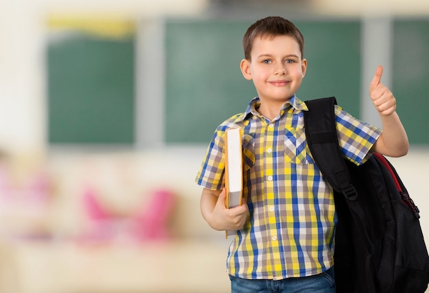 Schuljunge mit Buch und Rucksack, der Daumen nach oben zeigt