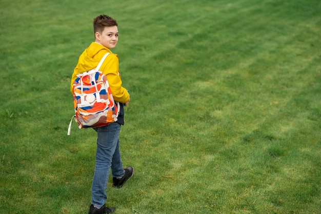 Schuljunge mit Rucksack geht auf grünem Rasen