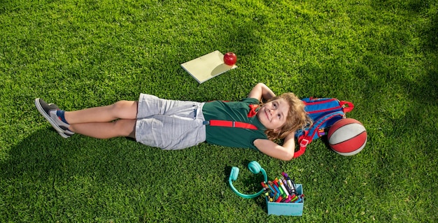 Schuljunge mit Schulmaterial in der Natur Fernlernen von Kindern Studieren Arbeiten Internet Kindererziehung Draufsicht auf kleinen Jungen, der auf grünem Gras liegt