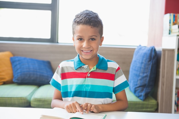 Schuljunge sitzt auf Tisch und liest Buch in Bibliothek