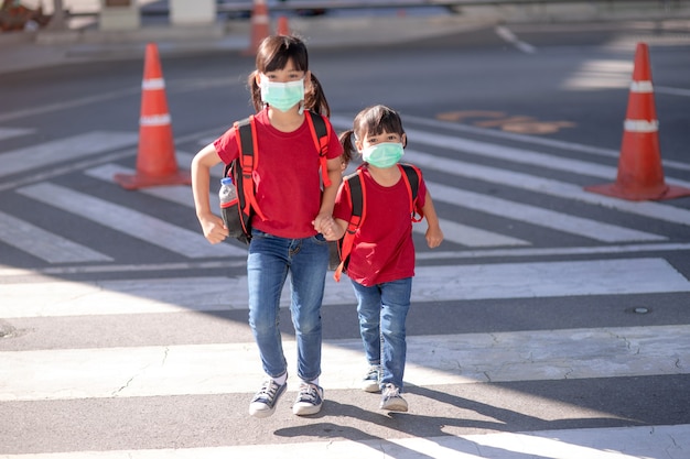 Schulkind, das während des Ausbruchs von Coronavirus und Grippe eine Gesichtsmaske trägt. Geschwistermädchen, das nach der Quarantäne und Sperrung von Covid-19 wieder zur Schule geht. Kinder in Masken zur Vorbeugung von Coronaviren.