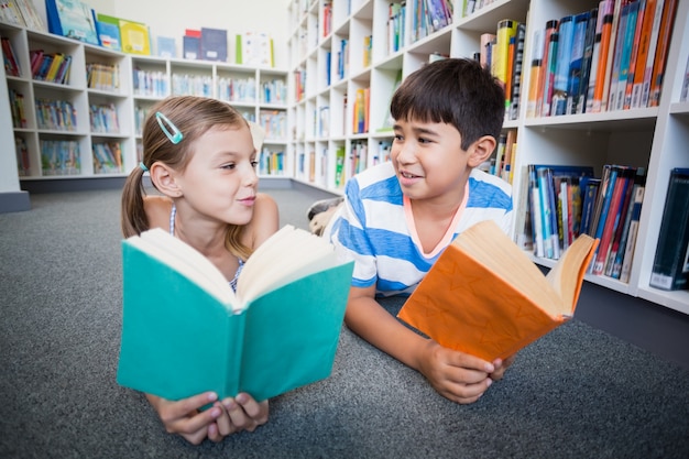 Schulkinder, die auf Boden liegen und ein Buch in der Bibliothek lesen