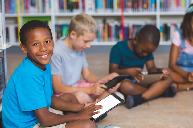 Schulkinder, die auf Boden mit digitalem Tablett in Bibliothek sitzen