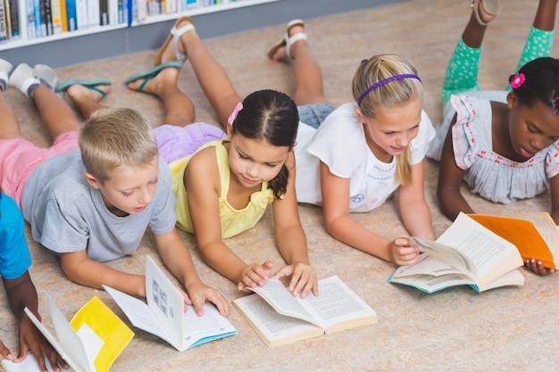 Schulkinder, die auf dem boden liegen und buch in der bibliothek lesen