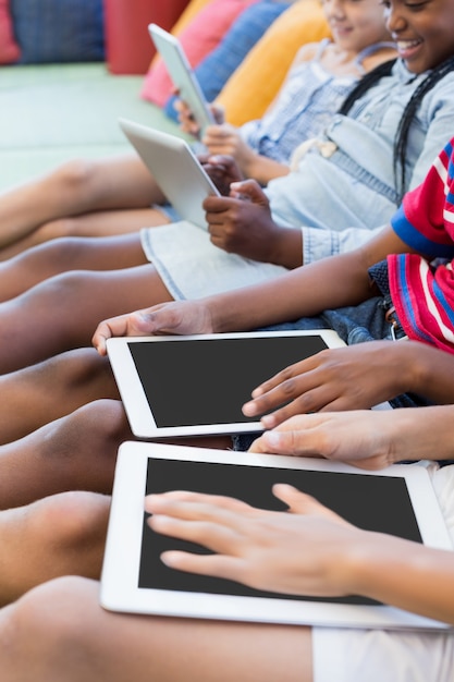 Schulkinder, die auf Sofa sitzen und digitale Tablette in der Bibliothek verwenden