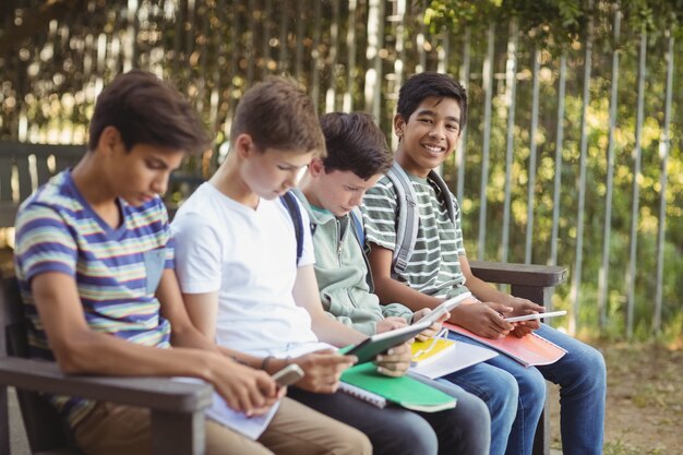 Schulkinder, die Handy und digitales Tablet auf Bank verwenden