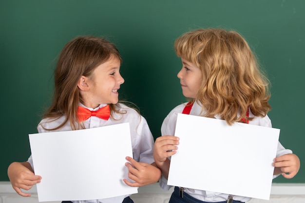 Schulkinder, die leeres Plakat des weißen Papiers mit Kopienraum halten glückliche Schulfreunde des Mädchens und des Jungen stellen p gegenüber