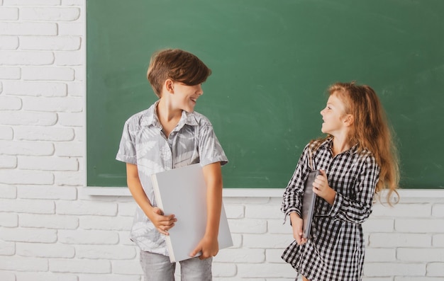 Schulkinder halten Buch mit überraschendem Ausdruck gegen Tafel Schulkinderfreunde