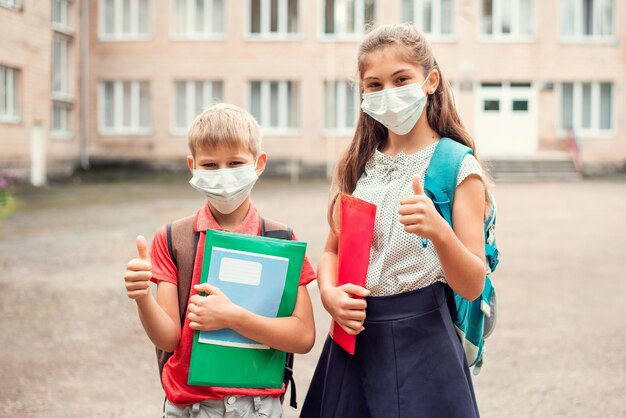 Schulkinder in medizinischen Masken vor dem Unterricht mit Daumen hoch