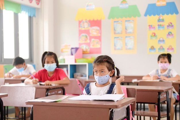 Schulkinder mit Schutzgesichtsmaske gegen Grippevirus im Unterricht im Klassenzimmer