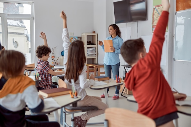 Schulkinder sitzen am Schreibtisch im Klassenzimmer und heben die Hände