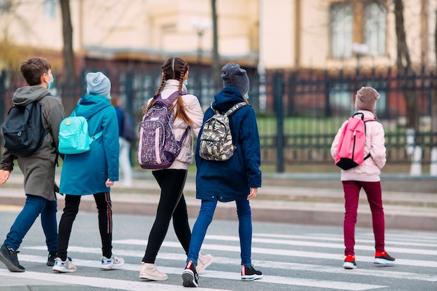 Schulkinder überqueren die Straße in medizinischen Masken. Kinder gehen zur Schule.