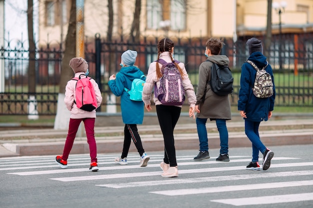 Schulkinder überqueren die Straße in medizinischen Masken. Kinder gehen zur Schule.