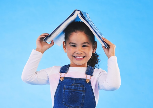 Schulleiter und Porträt eines Kindes mit Buch für Wissen oder Lernen, isoliert vor einem studioblauen Hintergrund. Kluges, kluges und junges Mädchen mit Notizbuch, das sich über Bildung, Geschichte oder Lesen freut