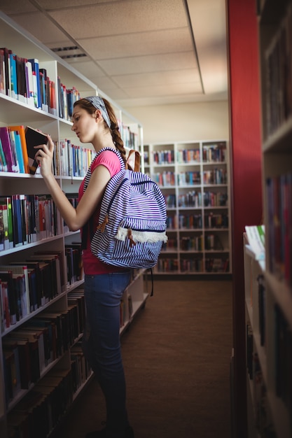 Schulmädchen, das Buch in der Bibliothek auswählt