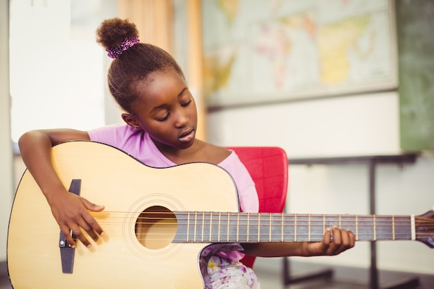 Schulmädchen, das Gitarre im Klassenzimmer spielt