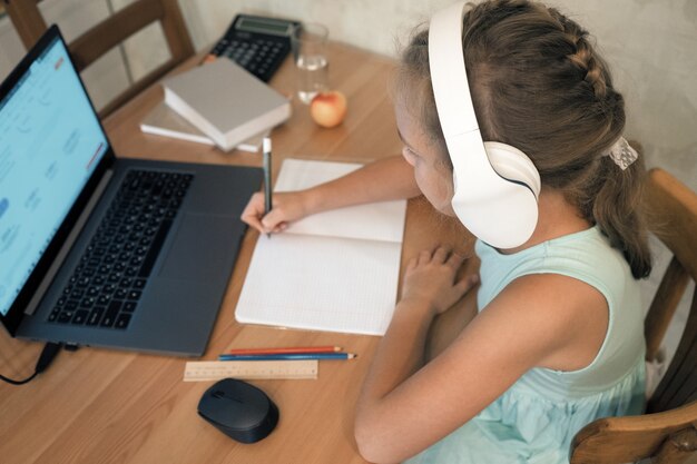 Schulmädchen, das zu Hause mit Laptop und Kopfhörern selektiven Fokus studiert
