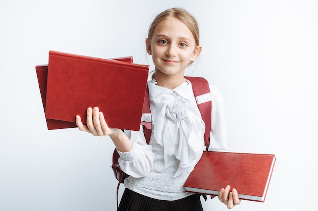 Schulmädchen des kleinen Mädchens, das ein Buch an einer weißen Wand hält