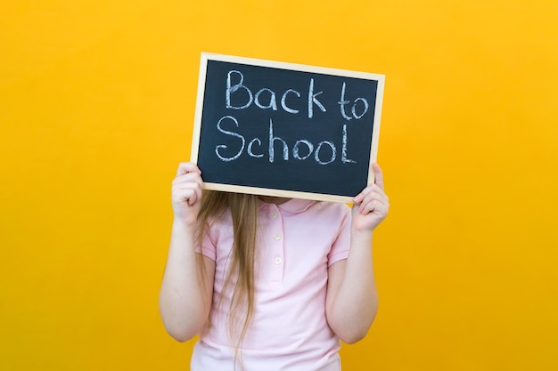 Foto schulmädchen hält ein tablet in den händen mit der aufschrift zurück zur schule auf gelbem hintergrund