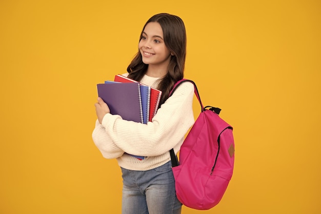 Schulmädchen hält Heft und Buch auf gelbem, isoliertem Studiohintergrund. Schul- und Bildungskonzept. Teenager-Mädchen in Schuluniform. Glückliches Gesicht, positive und lächelnde Emotionen des Teenager-Mädchens