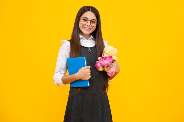 Schulmädchen halten Spielzeug Schulkinder mit Lieblingsspielzeug auf gelb isoliertem Hintergrund Konzept der Kindheit Glückliches Schulmädchen, positive und lächelnde Emotionen