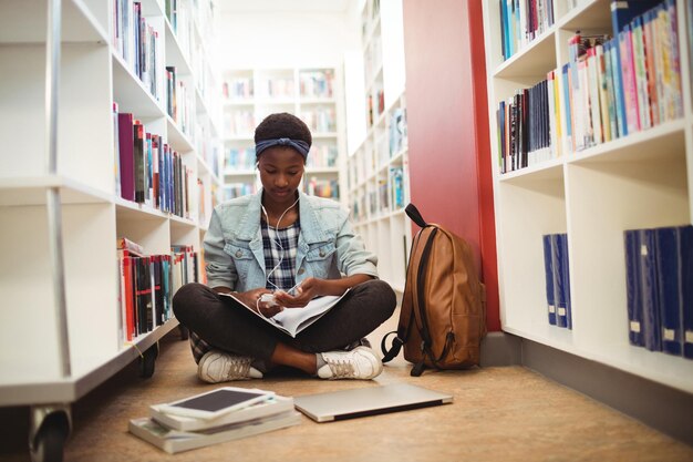 Schulmädchen hört Musik über Kopfhörer in der Bibliothek