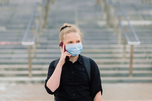 Schulmädchen in der medizinischen Schutzmaske bei Sonnenuntergang. Moderner Schüler mit Rucksack während der COVID-19-Quarantäne.