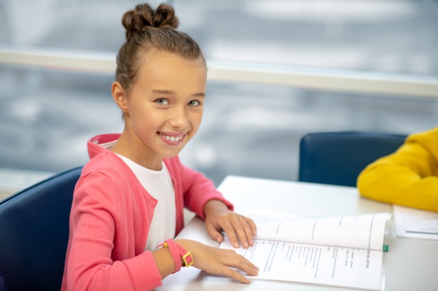 Schulmädchen lächelnd am Schreibtisch sitzen während ihrer Lektion