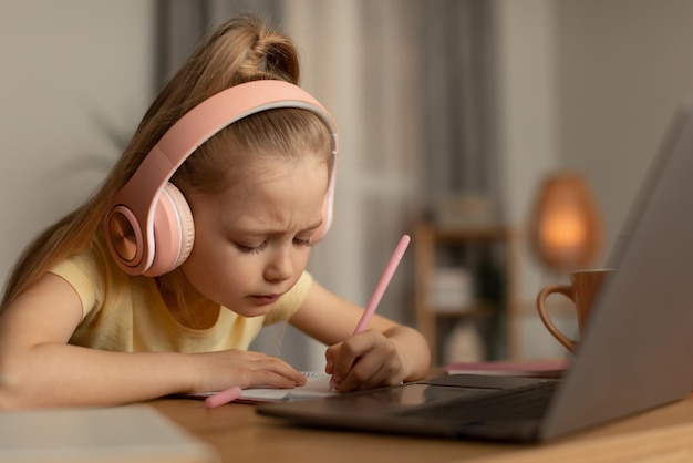 Schulmädchen macht sich Notizen und macht Hausaufgaben online mit Laptop zu Hause