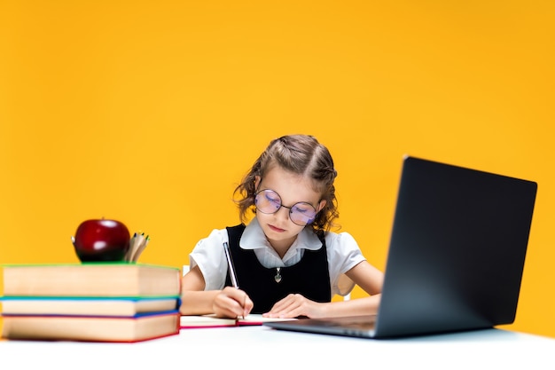 Schulmädchen mit Brille, das während des Online-Unterrichts Fernunterricht am Laptop schreibt und sitzt