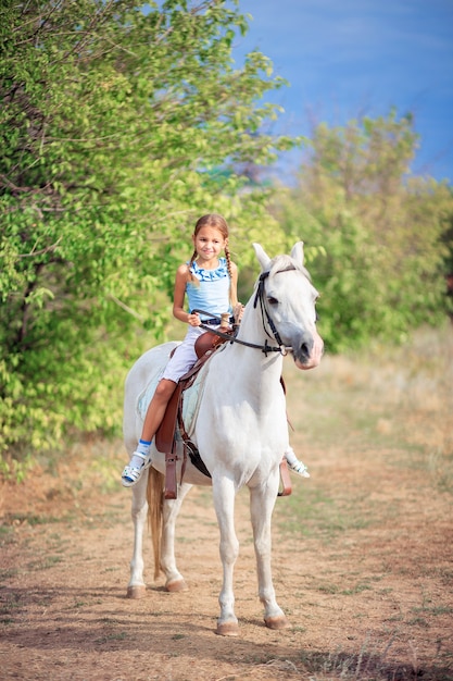 Schulmädchen reitet ein weißes Pony. Ein Kind reitet auf einem Pferd