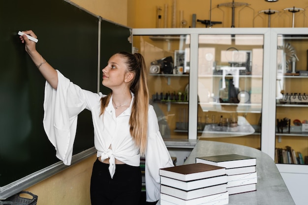 Schulmädchen schreibt mit Kreide auf Tafel Bildung in der Schule Ausgezeichneter Schüler mit vielen Büchern studieren an der Schulbehörde