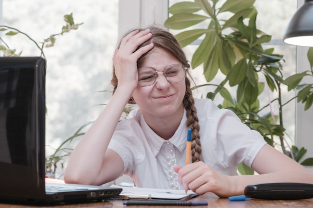 Schulmädchen-Selbstisolation mit Laptop für seine Hausaufgaben. Spiel-, Bildungs- und Schulkonzept - trauriges Mädchen mit Laptop und zu Hause. Mädchen, die es schwer haben, online Hausaufgaben zu machen und drinnen deprimiert zu sitzen