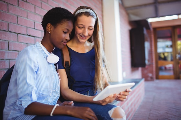 Schulmädchen sitzen gegen Backsteinmauer und verwenden digitales Tablet