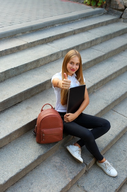 Schulmädchen sitzt auf der Treppe Daumen hoch