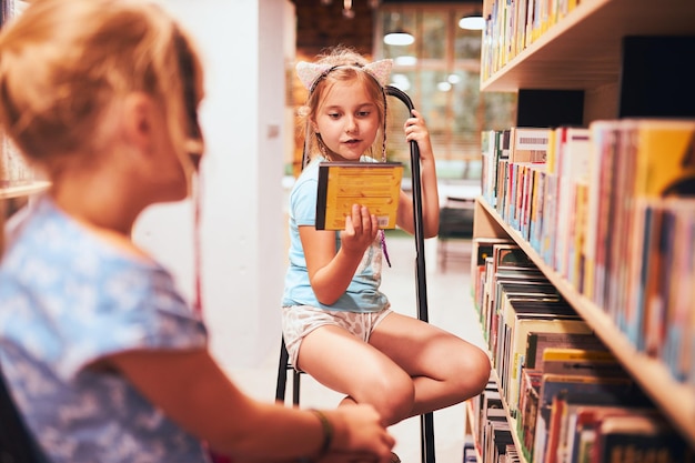 Foto schulmädchen suchen hörbücher in der schulbibliothek, schüler wählen bücher aus, grundschulbildung