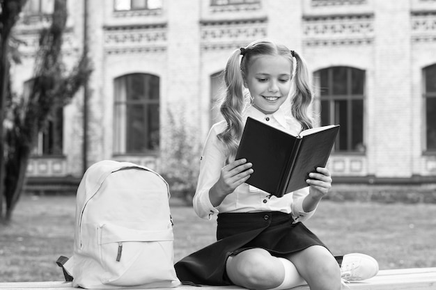 Schulmädchen süßes Kind mit Rucksack entspannen sich im Freien und lesen Buchkonzept