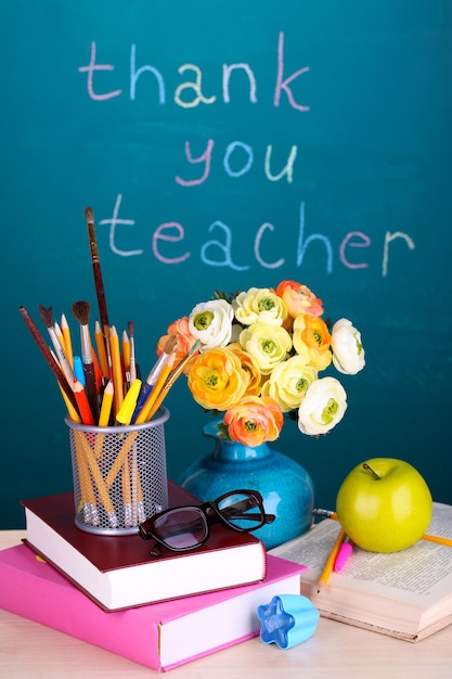 Schulmaterial und Blumen auf Tafelhintergrund mit der Aufschrift Danke Lehrer