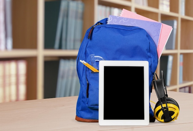 Schulrucksack mit Tablet und Kopfhörern auf dem Tisch