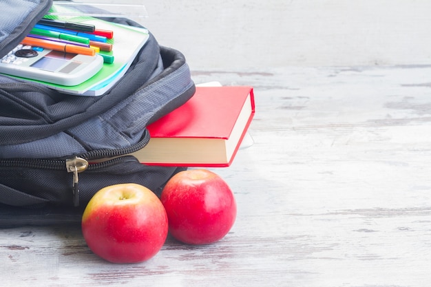 Schulrucksack mit Vorräten und Äpfeln auf weißem Holzdesktop