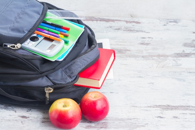 Schulrucksack mit Vorräten und Äpfeln auf weißem Schreibtisch