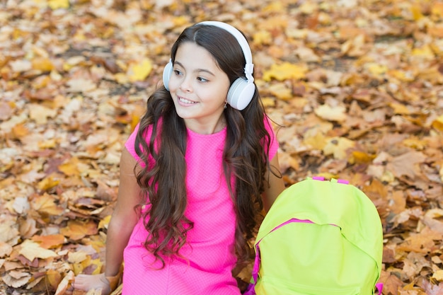 Schulzeit. zurück zur Schule. moderne Bildung. Kind mit Rucksack im Herbstwald. Konzept des Wissenstages. Kind im Herbstpark. glückliches Kind entspannt sich im Herbstlaub. kleines Mädchen trägt Kopfhörer.