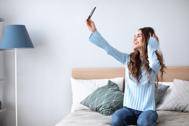 Schuss einer glücklichen jungen Frau, die selfie mit ihrem Handy nimmt, während sie im Wohnzimmer sitzt. Lebensstil.