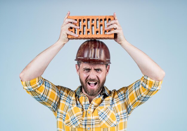 Schutzausrüstung reifer Bauarbeiter im Hemd unrasierter Mann auf der Baustelle gutaussehender Bauarbeiter mit Schutzhelm Tag der Arbeit wütender Typ trägt Schutzhelm hält Ziegelsteiningenieur bei der Arbeit